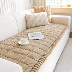 a white couch sitting next to a window in a living room with a coffee cup on top of it