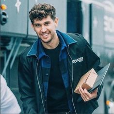 a man is walking down the street with a pizza box in his hand and smiling