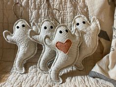 three white ghost ornaments hanging from a string on a quilted bed with a pillow in the background