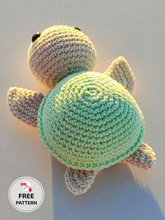 a crocheted turtle laying on the ground with its head turned to the side