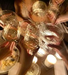 several people are holding wine glasses at a table with food and candles in front of them