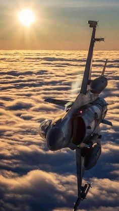 a fighter jet flying above the clouds at sunset