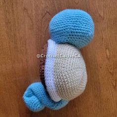 a crocheted blue and white stuffed animal sitting on top of a wooden floor