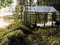 a small glass house in the middle of some grass and trees with sun shining on it