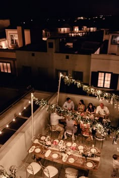 an overhead view of people sitting at tables on a rooftop with lights strung over them