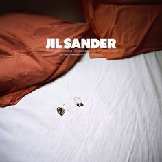 two earrings are laying on top of an unmade bed with the words jil sander above them