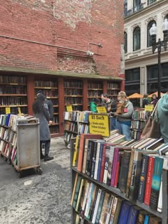 people browse books at an open air book market on the street in front of a brick building