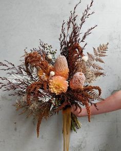 a person holding a bouquet of flowers in their left hand, against a white wall