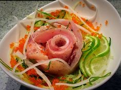 a white bowl filled with meat and vegetables on top of a marble countertop next to sliced cucumbers