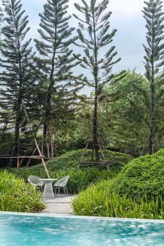 a chair and table by the edge of a swimming pool with trees in the background