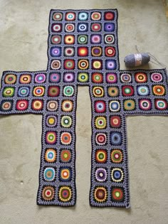 a crocheted cross is laying on the floor next to a ball of yarn