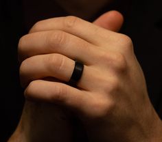 a man wearing a black wedding band with a ring on his finger, in the dark