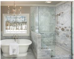 a white bath tub sitting under a window next to a sink and shower stall with a chandelier