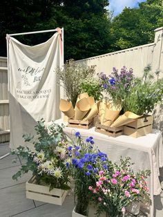 an outdoor table with flowers and hats on it's tables cloths are hanging from the fence