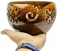 a hand holding a wooden bowl in it's left hand, with intricate designs on the outside