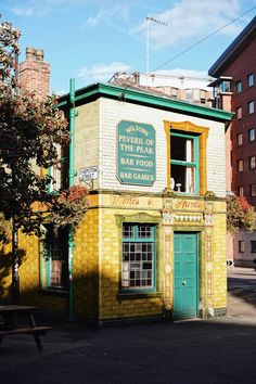 an old brick building with a green door and window on the outside, next to a park bench in front of it