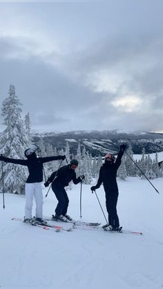 three people standing on skis in the snow with their arms up and one person wearing skis