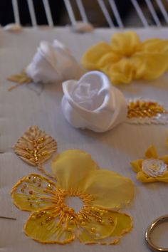 yellow and white fabric flowers on a table with two gold wedding rings next to them