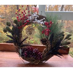 a wreath with berries and pine cones is sitting on a wooden table in front of a window