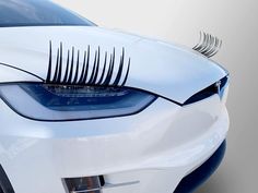 the front end of a white car with long black eyelashes on it