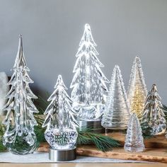 glass christmas trees sitting on top of a wooden table next to a white vase and pine tree