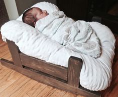 a baby wrapped in a blanket laying on top of a wooden bed