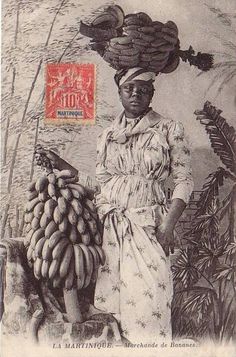 an old black and white photo of a woman carrying bananas