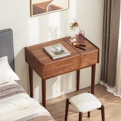 a small wooden desk with a magazine on it next to a bed in a bedroom