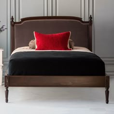 a bed with a red pillow on top of it next to a white table and two vases