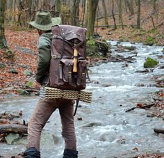 a man with a backpack crossing a stream in the woods on his hiking boots and hat