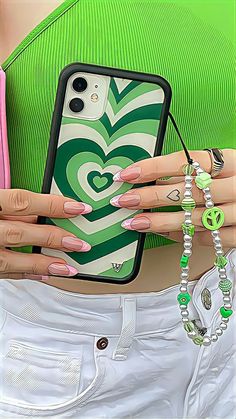 a woman holding her cell phone with green and white designs on the back, while wearing bracelets