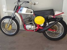 a red and white dirt bike parked in front of a garage door with a yellow seat