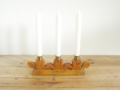 three candles are sitting on a stand with two white candles in the middle and one gold candle holder