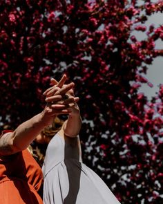 two people reaching out their hands in front of a tree with pink flowers on it