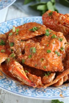 a blue and white plate topped with cooked crab legs covered in sauce, garnished with parsley