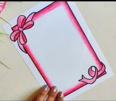 a person holding up a card with a pink ribbon on it and flowers in the background