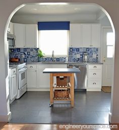 an archway leads into a kitchen with white cabinets and blue tile backsplashing