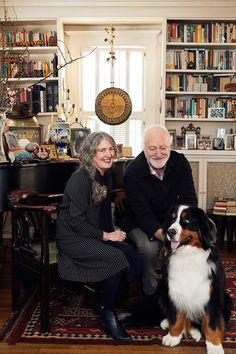 an older man and woman sitting next to a dog in front of a bookcase