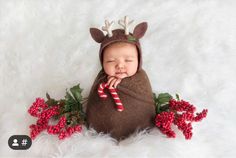 a newborn baby wearing reindeer antlers and holding a candy cane