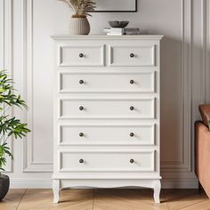 a white chest of drawers sitting next to a potted plant on top of a hard wood floor