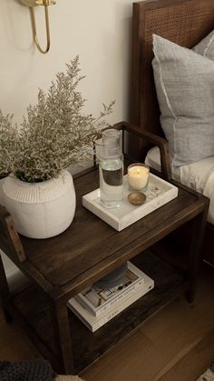 a small table with a candle and some books on it in front of a bed