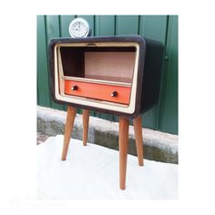 an old fashioned tv sitting on top of a wooden stand next to a green wall