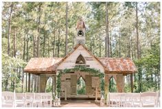 an outdoor wedding venue in the woods with white chairs and greenery on the ground