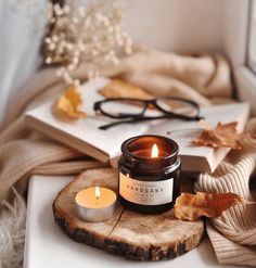 a candle sitting on top of a wooden slice next to a book and eyeglasses