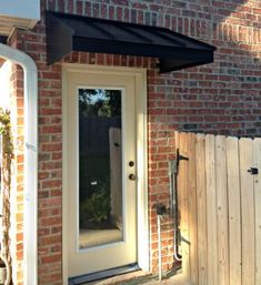 a door with a black awning over it next to a wooden fence and brick building