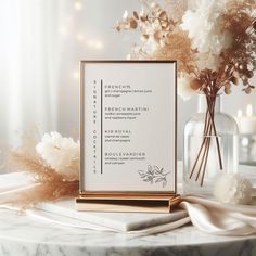 a white and gold wedding seating plan on a marble table with flowers in a vase