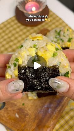 a woman holding up a sushi with rice and vegetables on it in front of a plate