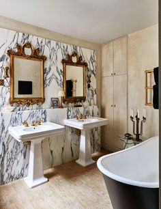 a bathroom with two sinks and a bathtub in the middle, surrounded by gold framed mirrors