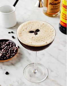 a close up of a drink in a wine glass on a table with coffee beans