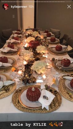 the table is set with white and gold plates, silverware, candles and pumpkins